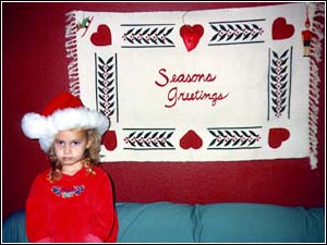 Image of a pouting girl wearing a Santa hat, standing in front of a 'Seasons Greetings' wall hanging...